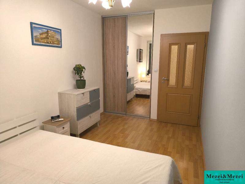 Ložnice v 2-pokojovém bytě s podlahou s dřevěným dekorem, skříně se zrcadlem a obrazem.