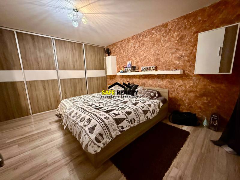 Ložnice v 2pokojovém bytě s postelí, úložným prostorem a podlahou s dřevěným dekorem.