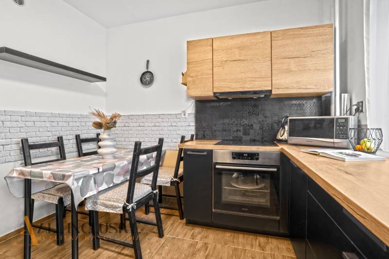 Kuchyně s dřevěným dekorem, jídelním stolem a spotřebiči ve 3pokojovém bytě.