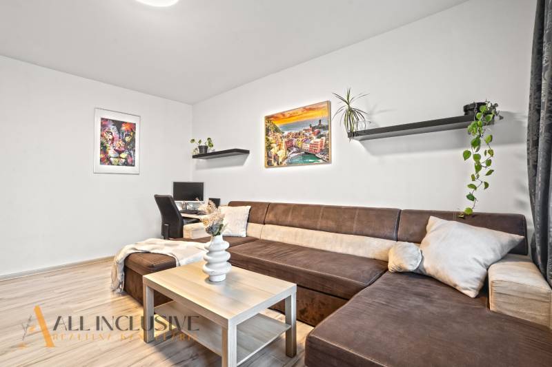 Obývací pokoj s hnědou sedačkou, pracovním stolem a podlahou s dřevěným dekorem.