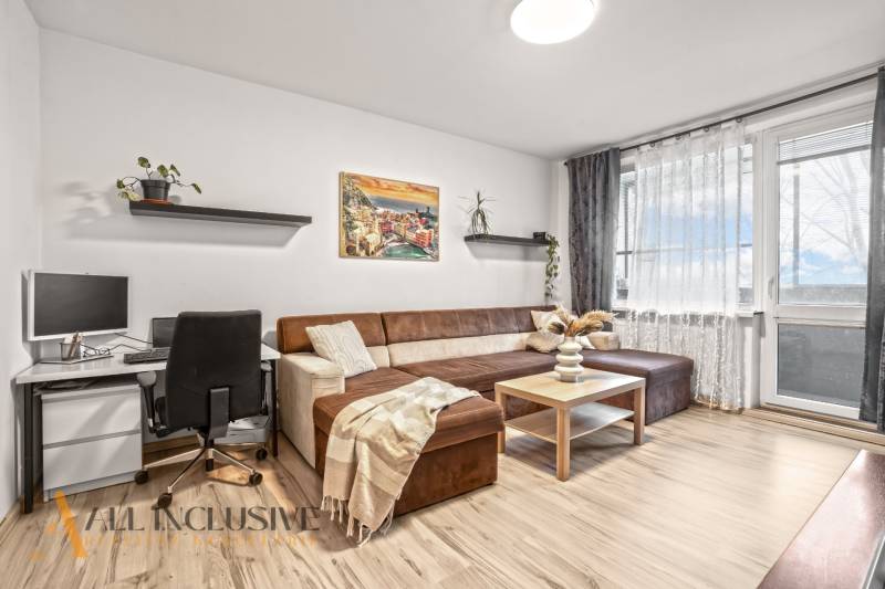 Obývací pokoj v 3-pokojovém bytě s pohovkou, pracovním stolem a podlahou s dřevěným dekorem.