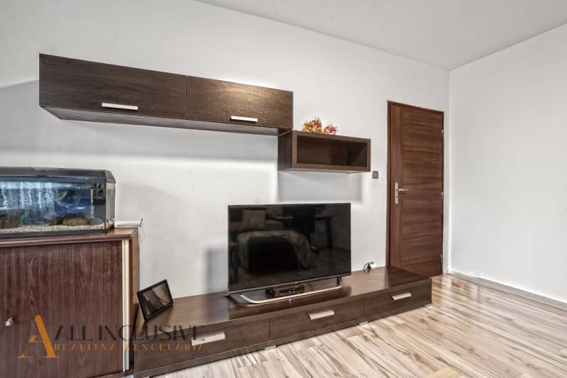 Obývací pokoj v 3pokojovém bytě s podlahou s dřevěným dekorem a velkou televizí.