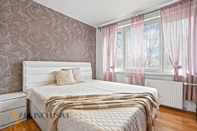 Ložnice v 3pokojovém bytě s dekorativní tapetou a podlahou s dřevěným dekorem.