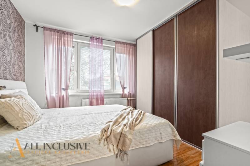 Ložnice v 3pokojovém bytě s postelí, skříní a dekorativními polštáři, podlaha s dřevěným dekorem.