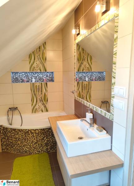 Koupelna v rodinném domě s vanou, umyvadlem, zrcadlem a mozaikovou výzdobou.