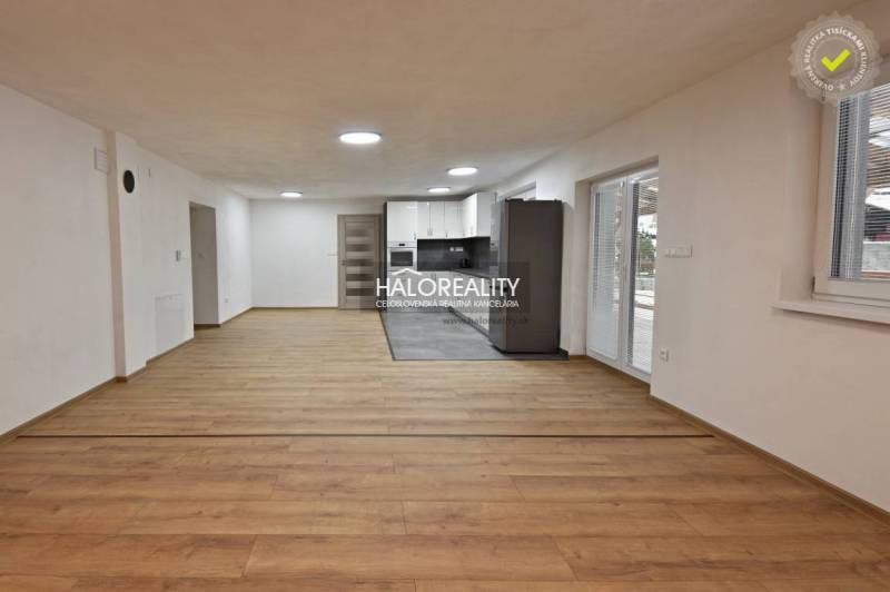 Obývací pokoj v rodinném domě s kuchyní, podlaha s dřevěným dekorem, bílé stěny.