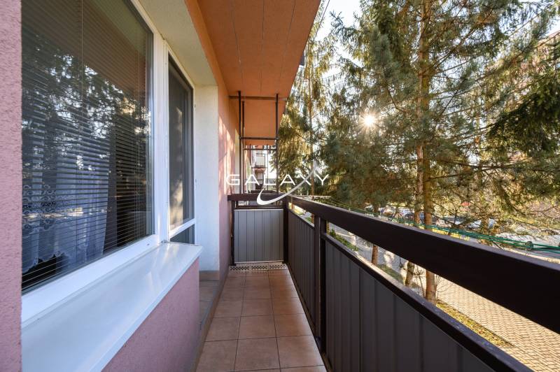 Balkon na Sládkovičově ulici ve Fiľakovu, obklopený zelení, součást 2-pokojového bytu.