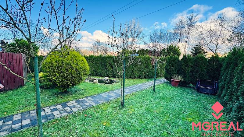 Zahrada u chaty v Partizánském s upraveným chodníkem a živým plotem.