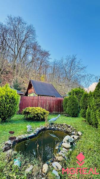 Chata v Partizánskem, obklopená zahradou s umělým jezírkem a sochami.