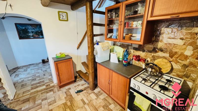 Kuchyně v chatě s dřevěným dekorem, schody, spotřebiči a nábytkem s kamennou stěnou.