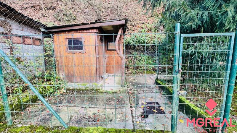 Dřevěná chata obehnaná kovovým plotem v lese u Partizánskeho.