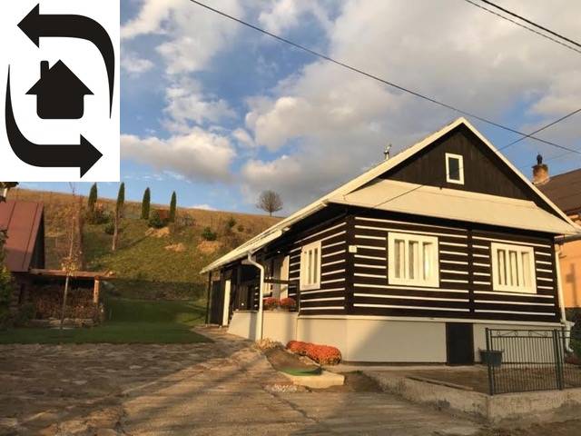 Chata v Legnavě s dřevěným obkladem a dlážděným dvorem, obklopená přírodou a kopci.