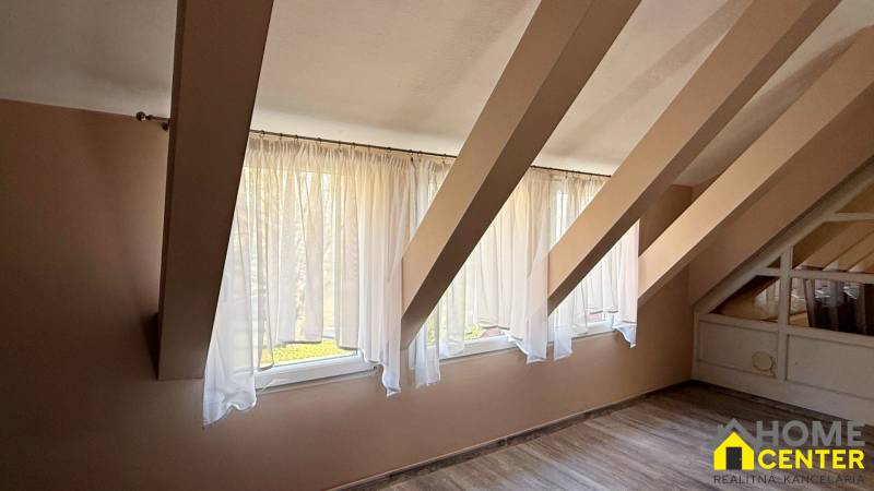 Interiér podkroví s okny a podlahou s dřevěným dekorem.