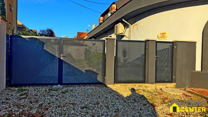 Kovová brána u budovy v Komárně na štěrkovém pozemku u domu.