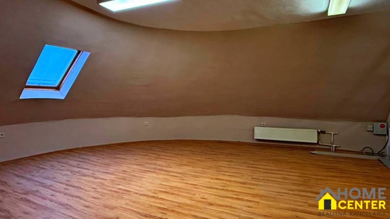 Podkrovní pokoj s oknem, radiátorem a podlahou s dřevěným dekorem.