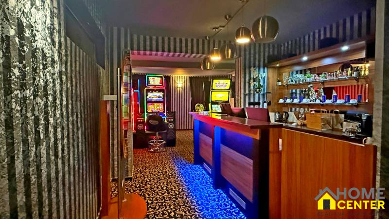 Interiér budovy s hracími automaty, pultem a nápoji na policích.