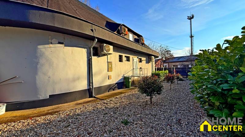 Budova v Komárně s klimatizací, kterou obklopuje štěrková plocha a keře.