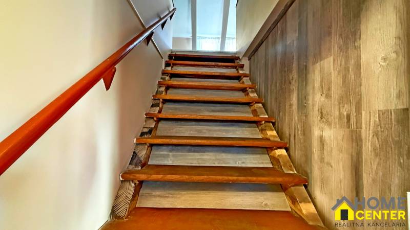 Schodiště s dřevěným zábradlím a podlahou s dřevěným dekorem vede do patra budovy.