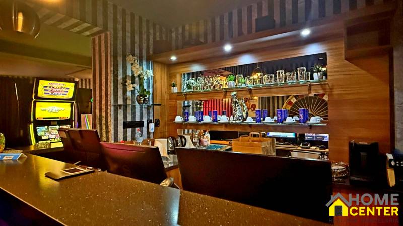 Interiér budovy s barovým pultem, ozdobnými regály a automatem.