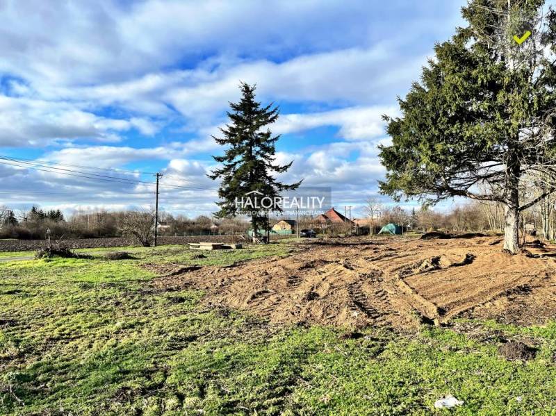 Pozemky na bydlení v Ondrejovcích s travnatou plochou a stromy pod modrou oblohou.