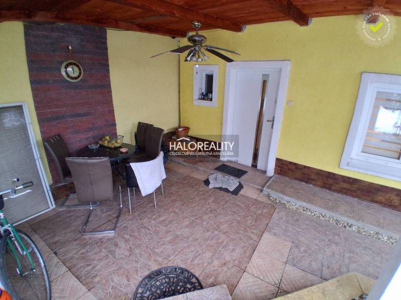 Terasa rodinného domu s dlažbou a sedacím nábytkem. Ve výklenku jsou stůl a hodiny.