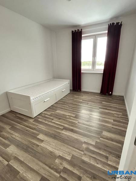 Pokoj s postelí, podlahou s dřevěným dekorem a velkým oknem ve 3pokojovém bytě.