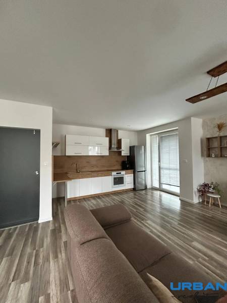 Obývací pokoj s kuchyňskou linkou a podlahou s dřevěným dekorem ve 3pokojovém bytě.