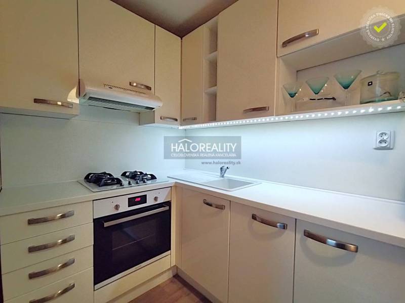 Kuchyně v 2-pokojovém bytě s bílými skříňkami, plynovým sporákem a úložným prostorem.