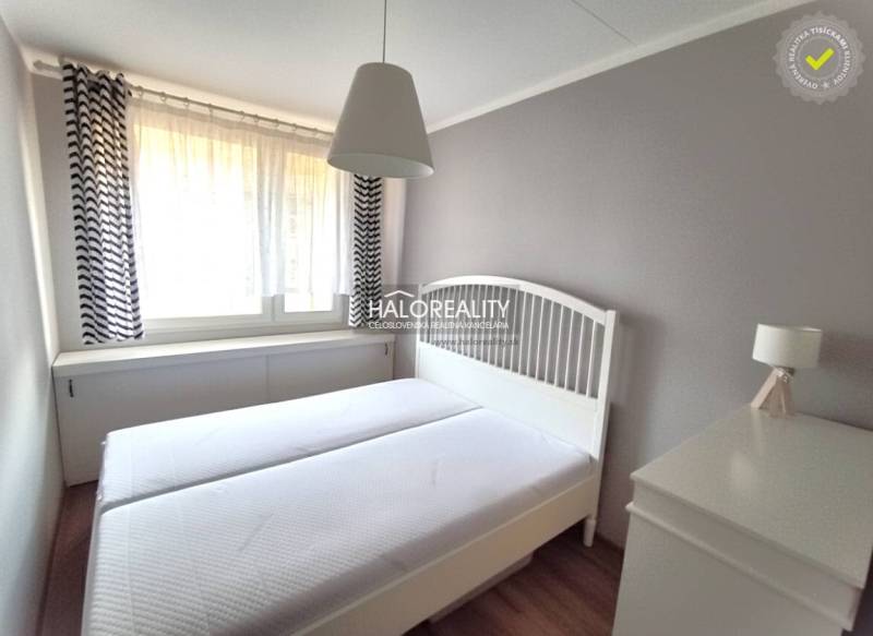 Ložnice v dvoupokojovém bytě s bílým nábytkem a jemnými závěsy.