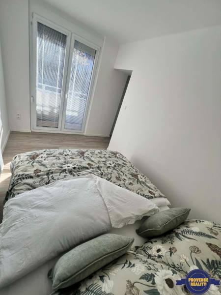 Světlá ložnice v 2-pokojovém bytě s dekorativními polštáři a podlahou s dřevěným dekorem.