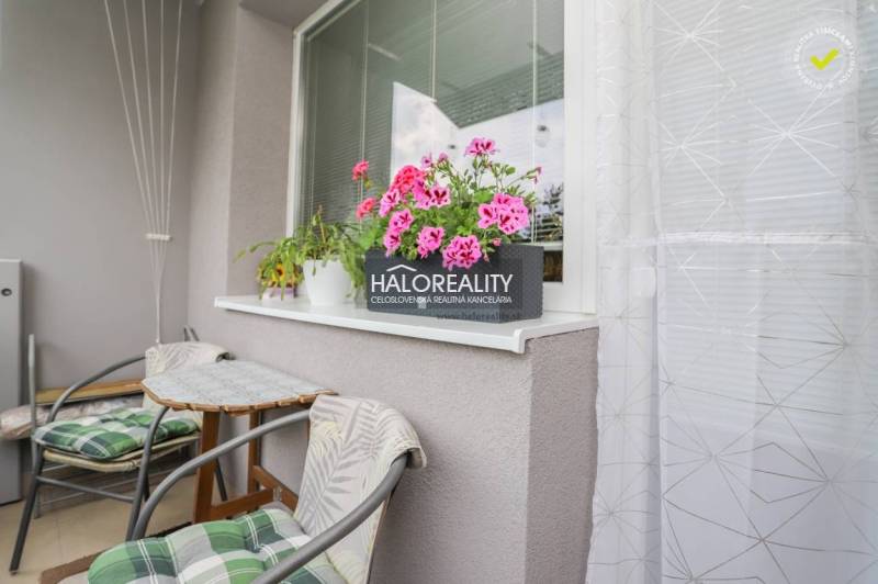 Balkon 3pokojového bytu s květinami a stolem, vhodný k relaxaci.