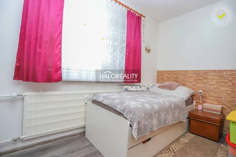 Pokoj v 3-pokojovém bytě s postelí, květinovým závěsem a podlahou s dřevěným dekorem.