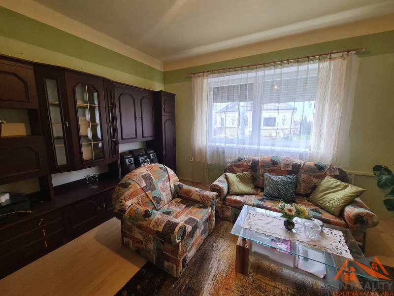 Obývací pokoj rodinného domu s barevnou pohovkou a tmavou obývací stěnou.