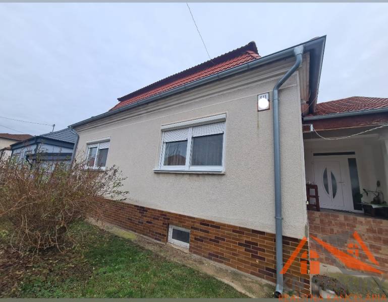 Rodinný dům v Hurbanově se světlou fasádou a červenou střechou, obklopený keři.