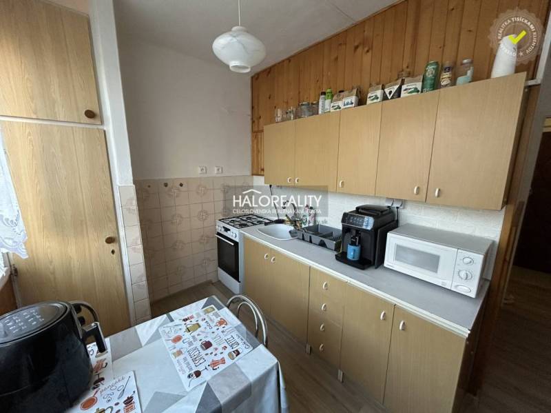 Kuchyně v 2-pokojovém bytě s dřevěným dekorem, včetně spotřebičů a jídelního stolu.