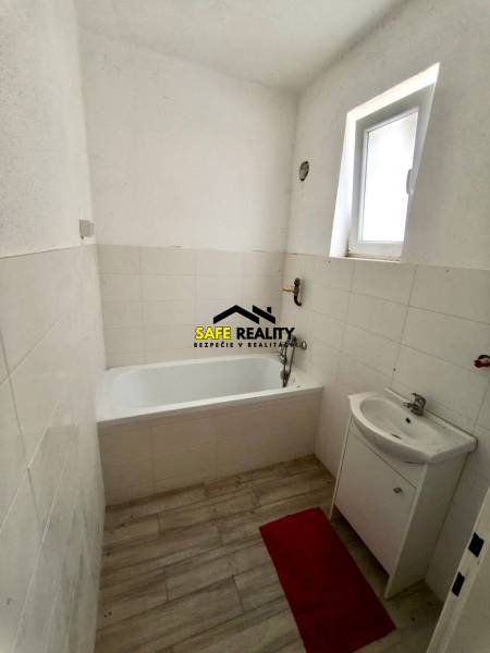 Koupelna v rodinném domě s vanou, umyvadlem a podlahou s dřevěným dekorem.