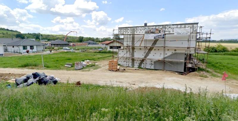 Stavební pozemek na bydlení v Modrovce s rozestavěnou budovou a okolím v pozadí.