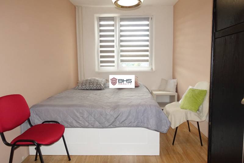 Ložnice v 3-pokojovém bytě s postelí, křesly a podlahou s dřevěným dekorem.