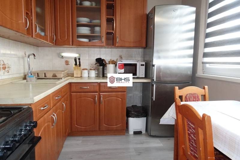 Kuchyně s dřevěným dekorem, sporákem, lednicí a jídelním stolem ve 3-pokojovém bytě.