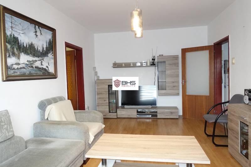 Obývací pokoj třípokojového bytu s pohodlnou pohovkou, nábytkem s dřevěným dekorem a televizorem.