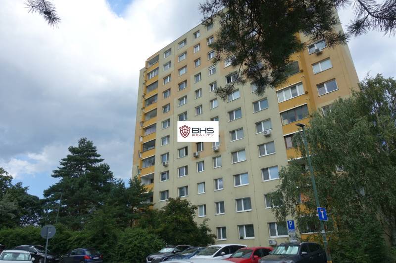 Bytový dům v Bratislavě-Dúbravce na Homolově ulici, obklopený stromy a parkovištěm.