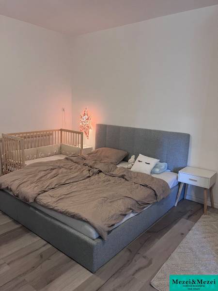 Ložnice s čalouněnou postelí, dětskou postýlkou a nočním stolkem ve 4pokojovém bytě.