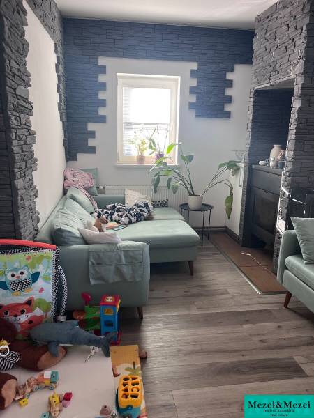 Obývací pokoj se zelenou sedačkou, hračkami, rostlinami a stěnami s kamenným obkladem ve 4pokojovém bytě.