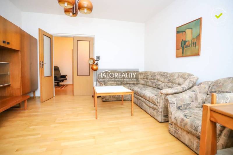 Obývací pokoj třípokojového bytu s pohovkou, stolem a podlahou s dřevěným dekorem.