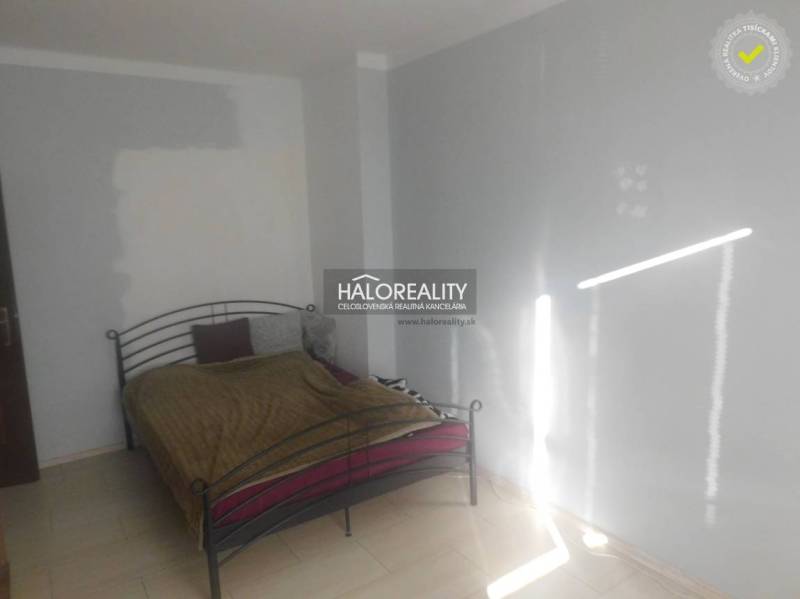 Ložnice s kovovou postelí a bílými stěnami v dvoupokojovém bytě.