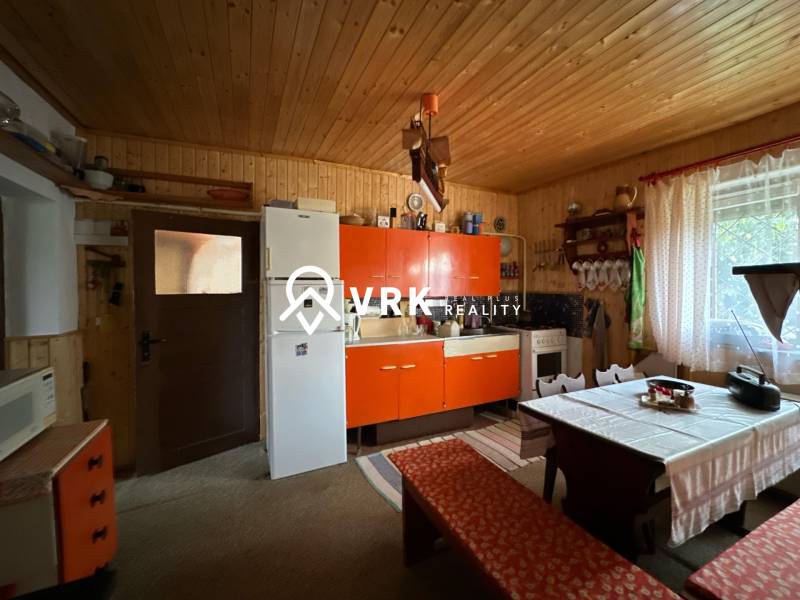 Kuchyně v rodinném domě se starožitným nábytkem, rustikální stěna, velké okno.