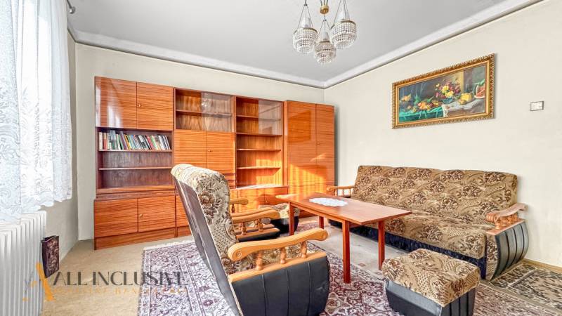 Obývací pokoj v rodinném domě s křesly, kobercem, knihovnou a závěsy.