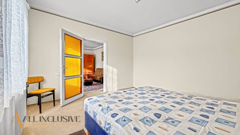 Ložnice v rodinném domě s postelí, křeslem a dveřmi s oranžovým sklem.