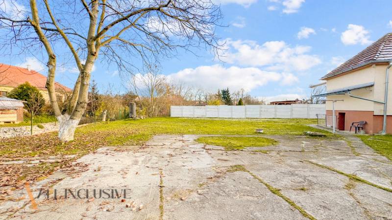 Dvůr u rodinného domu na Nemečkovské ulici v Prašicích s dlážděnou plochou a stromy.