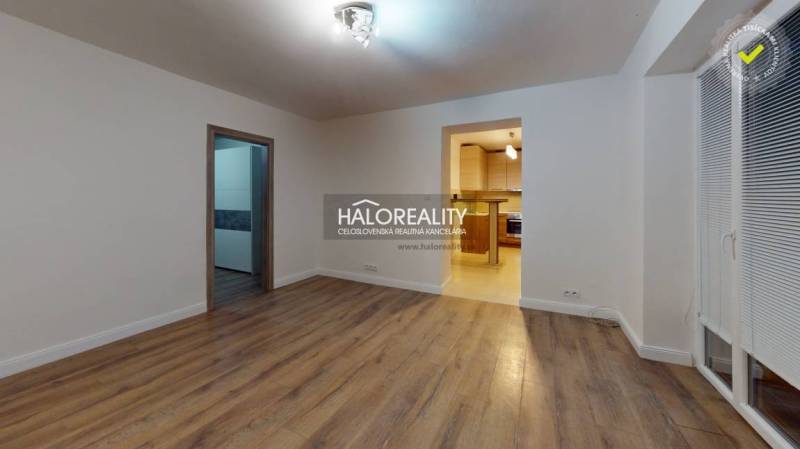 Obývací pokoj v dvoupokojovém bytě s podlahou s dřevěným dekorem a vstupem do kuchyně.